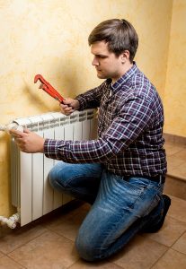 man with wrench preparing to work on radiator in home